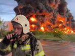 In this handout photo made from video released by the Governor of Sevastopol Mikhail Razvozhaev telegram channel on Saturday, April 29, 2023, a firefighter speaks on the walkie talkie as smoke and flame rise from a burning fuel tank in Sevastopol, Crimea. A massive fire erupted at an oil reservoir there after it was hit by a drone, a Russian-appointed official there reported on Saturday. (Sevastopol Governor Mikhail Razvozhaev telegram channel via AP)